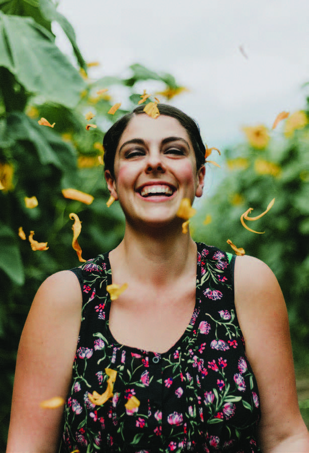 confetti falls through the air in front of a happy young woman surrounded by tall green plants