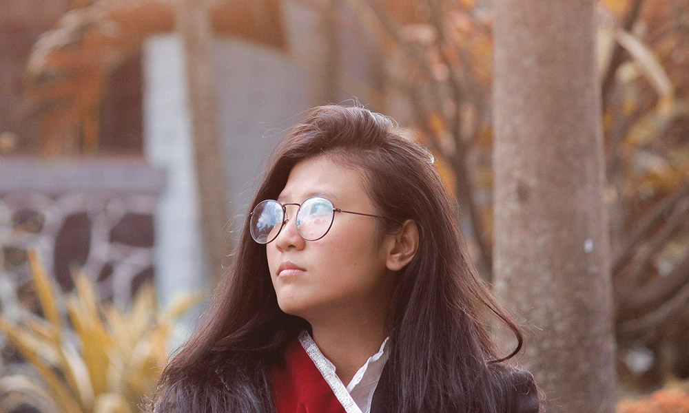 A young Asian-American woman wearing glasses looks to the side.