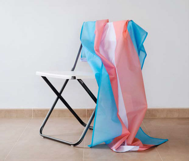 A trans flag draped over a folding chair.