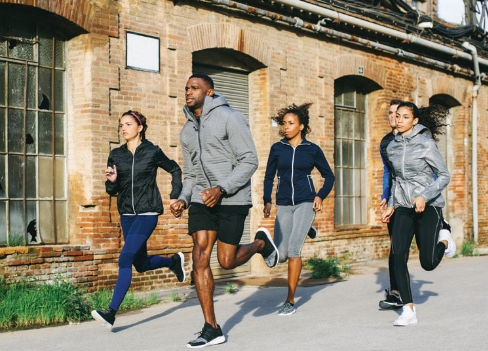 A multicultural group of young adults in modern gray and black running outfits runs together for exercise outdoors.