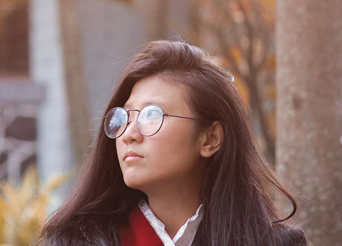 A young Asian-American woman wearing glasses looks to the side.