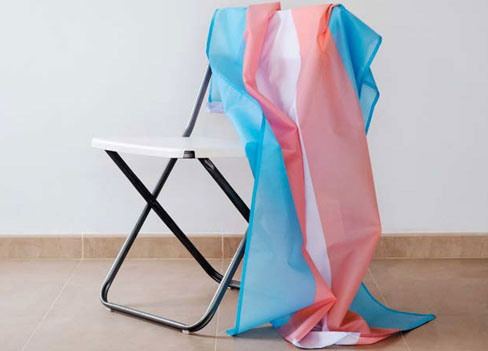 A trans flag draped over a folding chair.